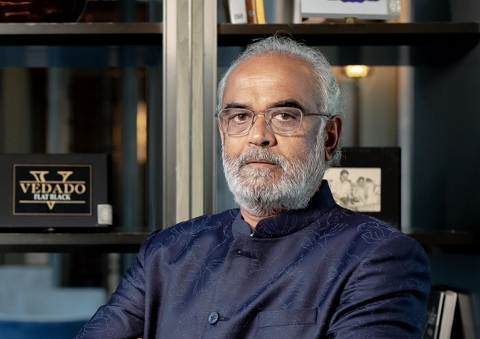 Savji Dholakia seated in an office, looking towards the camera, wearing a dark indigo bandhgala.