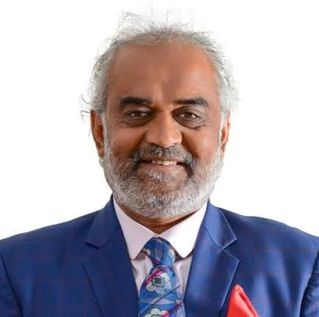 Formal portrait of Savji Dholakia in a blue suit against a plain background.
