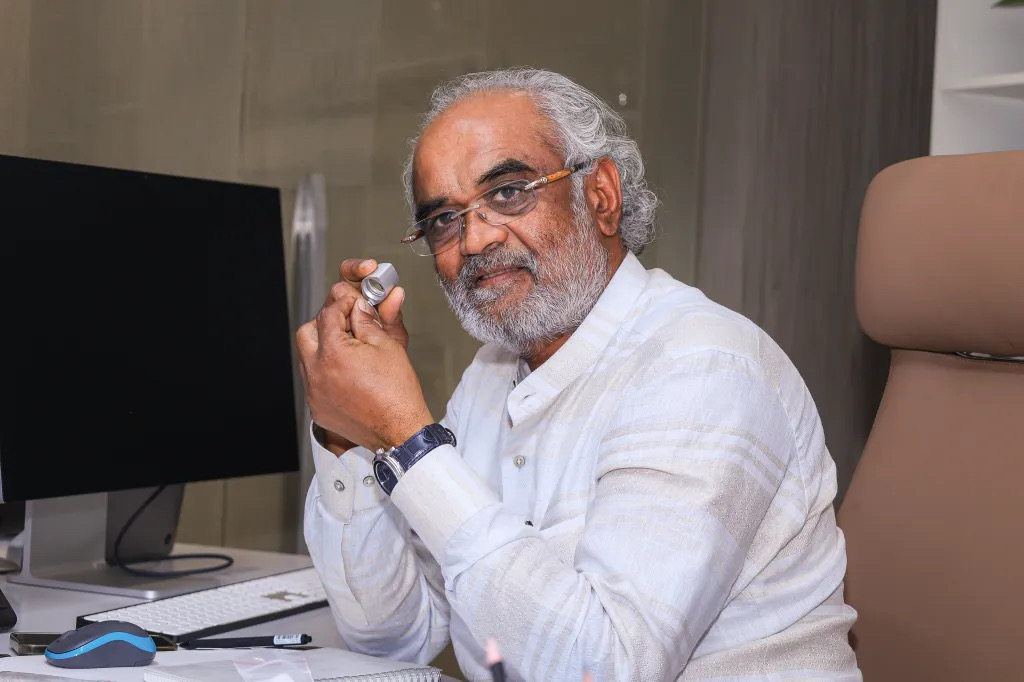 Savji Dholakia seated at his desk holding a jeweller&rsquo;s loupe to his eye.