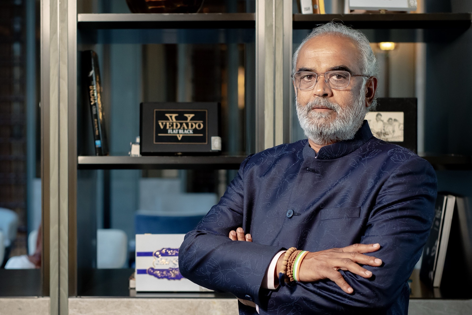 Savji Dholakia standing with his arms folded in his office, wearing a dark indigo bandhgala.