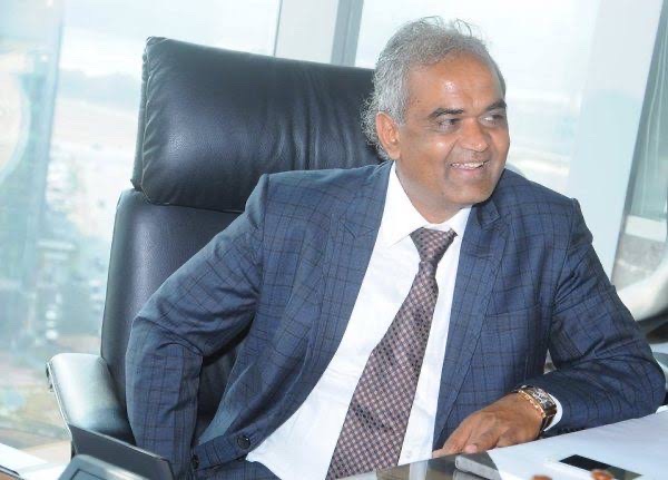 Savji Dholakia seated at his office desk in a blue checked suit.