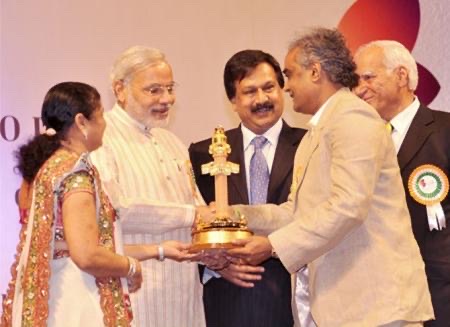 Savji Dholakia receiving an award trophy at a public ceremony.