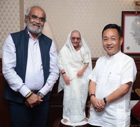 Savji Dholakia standing with an elderly woman and another guest during a formal visit.